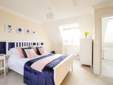 A bedroom with a white bed frame and blue and pink bedding a white cabinet with flowers and a window at Anchors Away in Weymouth