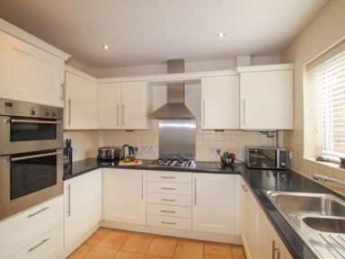 A kitchen with white cabinets black countertops double oven gas stove toaster kettle microwave and stainless steel sink at Anchors Away in Weymouth