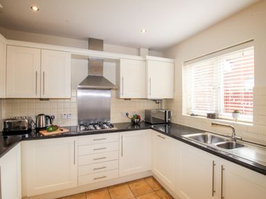 A kitchen with white cabinets black countertops a gas stove toaster kettle microwave and a window at Anchors Away in Weymouth