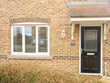 A front door and window of a brick house with a small awning above the door at Anchors Away in Weymouth