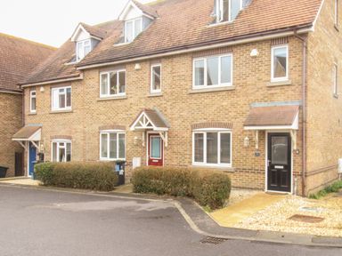 A row of brick townhouses with three front doors and windows with hedges and a paved driveway in front