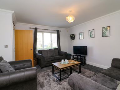 A living room with three gray sofas a wooden coffee table a TV on a stand and framed plant pictures on the wall at Anchors Away in Weymouth