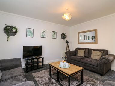 A living room with two sofas a wooden coffee table with cups a TV on a stand and framed botanical prints on the wall at Anchors Away in Weymouth