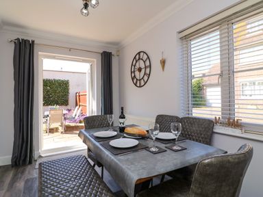 A dining room with a table set for four people next to a window and open door leading to a patio at Anchors Away in Weymouth