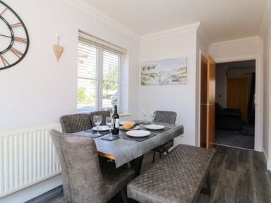 A dining area with a table set for four people with plates and glasses and a bench and chairs at Anchors Away in Weymouth