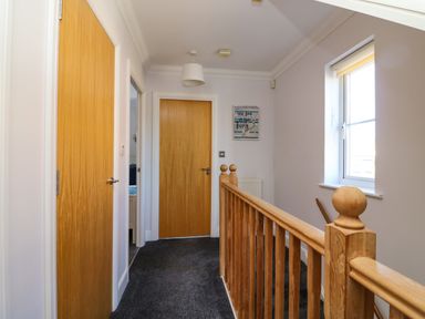 A hallway with wooden doors carpeted floor a wooden banister and a window at Anchors Away in Weymouth