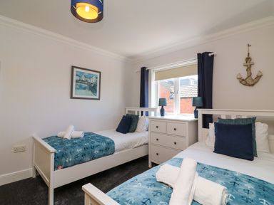 A bedroom with two single beds a dresser and a window at Anchors Away in Weymouth