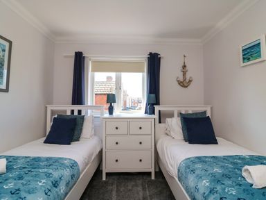 A bedroom with two single beds a white chest of drawers and a window at Anchors Away in Weymouth
