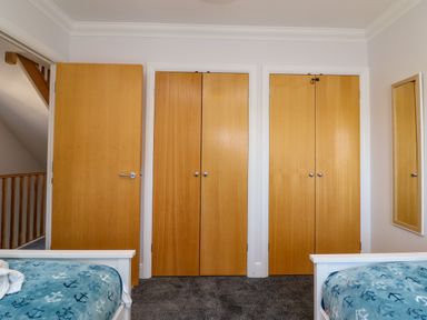 A bedroom with two beds covered in blue anchor patterned blankets three closed wooden doors a mirror on the wall and a hallway visible through an open door at Anchors Away in Weymouth