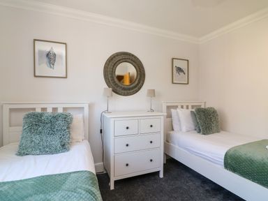 A bedroom with two single beds green cushions and blanket a white chest of drawers and round mirror at Anchors Away in Weymouth