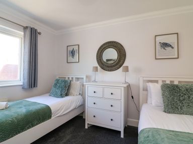 A bedroom with two single beds with green cushions and blankets a white chest of drawers and a round mirror at Anchors Away in Weymouth