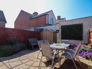 A garden patio with a table and chairs surrounded by flowers and a wooden shed at Anchors Away in Weymouth