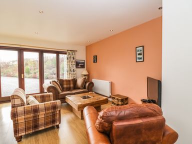 A living room with sofas a wooden coffee table a television and glass doors at The Lodge in Dol-y-Gaer near Pontsticill