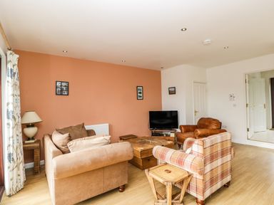 A living room with sofas a TV and wooden tables at The Lodge in Dol-y-Gaer near Pontsticill