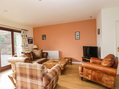 A living room with three armchairs a wooden coffee table a television and a window with curtains at The Lodge in Dol-y-Gaer near Pontsticill