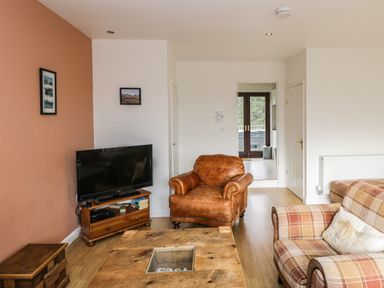 A living room with a leather armchair a plaid sofa a wooden coffee table and a television on a wooden stand at The Lodge in Dol-y-Gaer near Pontsticill