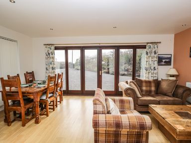 A dining area with wooden table and chairs and a living area with plaid and brown couches at The Lodge in Dol-y-Gaer near Pontsticill