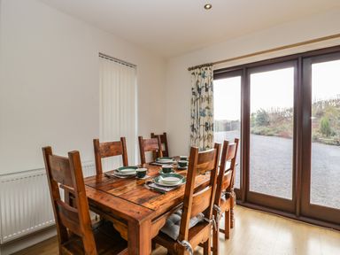 A dining room with a wooden table and six chairs set with dishes near glass doors at The Lodge in Dol-y-Gaer near Pontsticill