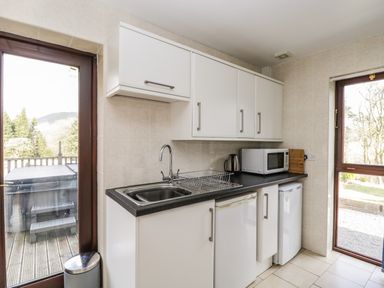 A kitchen with white cabinets black countertop stainless steel sink microwave kettle and two windows at The Lodge in Dol-y-Gaer near Pontsticill
