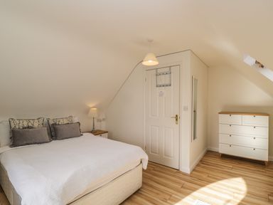 A bedroom with a bed a bedside table with a lamp a door a mirror and a chest of drawers at The Lodge in Dol-y-Gaer near Pontsticill