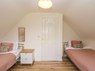 A bedroom with two single beds a nightstand and a door at The Lodge in Dol-y-Gaer near Pontsticill