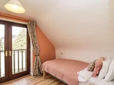 A small bedroom with a single bed near wooden French doors opening to a balcony at The Lodge in Dol-y-Gaer near Pontsticill