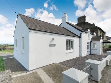 A white cottage with a grey roof and stone chimney under a blue sky at Morlan Cottage in Newport Pembrokeshire