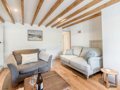 A living room with two sofas a wooden table with a wine bottle and glasses and exposed wooden ceiling beams at Morlan Cottage in Newport Pembrokeshire