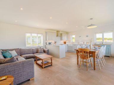 An open plan living room with a gray sofa wooden coffee table kitchen with white cabinets and a wooden dining table with chairs at Morlan Cottage in Newport Pembrokeshire