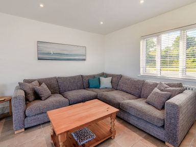 A living room with a grey corner sofa with cushions a wooden coffee table and a window with blinds at Morlan Cottage in Newport Pembrokeshire