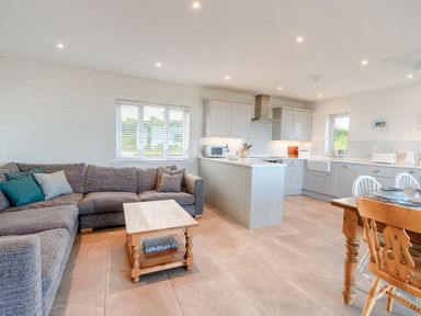 An open living room and kitchen with a gray sofa a wooden coffee table kitchen island and dining table at Morlan Cottage in Newport Pembrokeshire