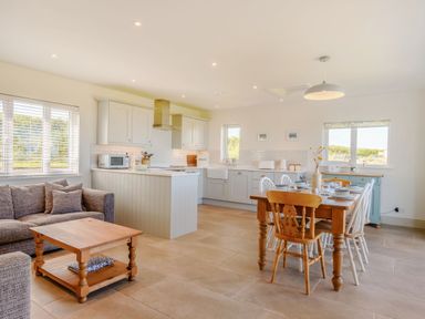 An open plan kitchen and dining area with a wooden dining table and chairs a grey sofa and a coffee table at Morlan Cottage in Newport Pembrokeshire