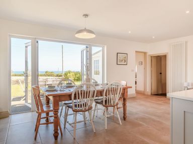 A dining area with a wooden table and chairs near glass doors opening to a garden at Morlan Cottage in Newport Pembrokeshire