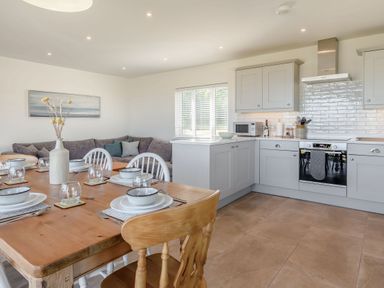 A kitchen and dining area with a wooden table set with dishes and a grey sectional sofa in the corner at Morlan Cottage in Newport Pembrokeshire