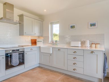 A kitchen with white cabinets a sink toaster kettle and bread box at Morlan Cottage in Newport Pembrokeshire