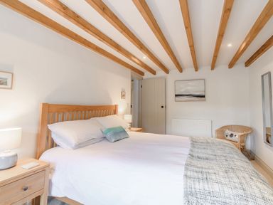 A bedroom with a wooden bed frame bedside tables lamps a wicker chair and wall art at Morlan Cottage in Newport Pembrokeshire