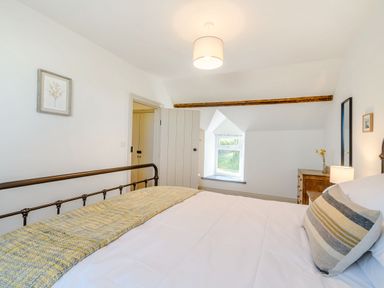 A bedroom with a metal bed frame a window a wooden dresser and framed pictures at Morlan Cottage in Newport Pembrokeshire