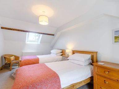 A bedroom with two single beds with orange blankets a wicker chair a wooden chest of drawers and a skylight window at Morlan Cottage in Newport Pembrokeshire