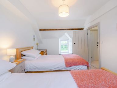 A bedroom with two single beds with orange throws a wooden chest of drawers a bedside table with a lamp and a small window at Morlan Cottage in Newport Pembrokeshire