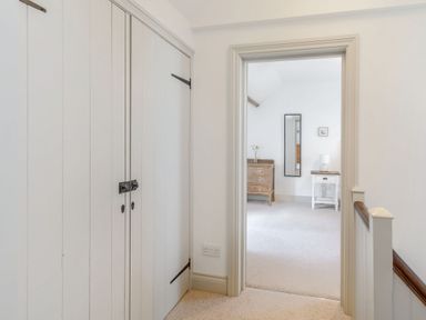 A hallway with built in cupboards leading to a room with a wooden dresser a small white side table with a lamp and a wall mirror at Morlan Cottage in Newport Pembrokeshire