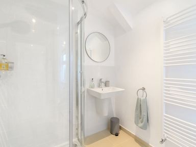 A bathroom with a shower cubicle a round mirror a wall-mounted sink a towel on a ring and a white heated towel rail at Morlan Cottage in Newport Pembrokeshire