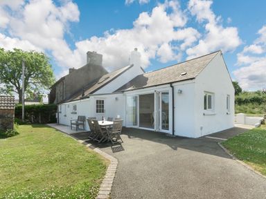 A white cottage with outdoor dining table and chairs on a driveway at Morlan Cottage in Newport Pembrokeshire