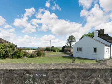 A white cottage with a garden and stone wall under a blue sky with clouds at Morlan Cottage in Newport Pembrokeshire