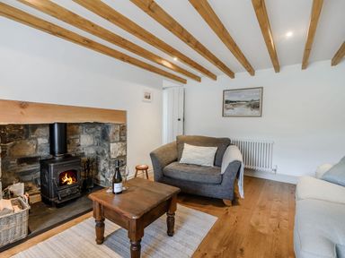 A living room with a wood burning stove stone fireplace gray armchair wooden coffee table and exposed ceiling beams at Morlan Cottage in Newport Pembrokeshire