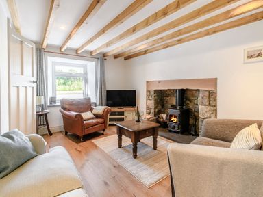 A living room with exposed wooden beams a wood burning stove a leather armchair and a sofa at Morlan Cottage in Newport Pembrokeshire