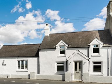 A white cottage with a brown roof and multiple windows under a blue sky at Morlan Cottage in Newport Pembrokeshire