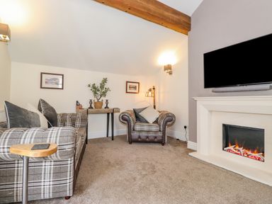 A living room with plaid sofas a fireplace a mounted tv and a small wooden table at Chestnuts Cottage in Windermere