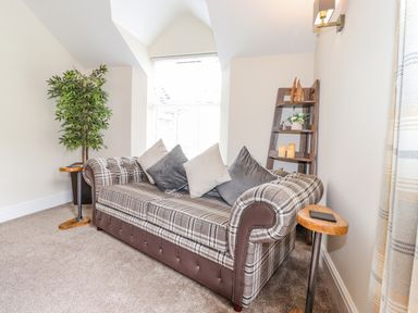 A sitting area with a plaid sofa cushions plant small tables and a wooden shelf at Chestnuts Cottage in Windermere