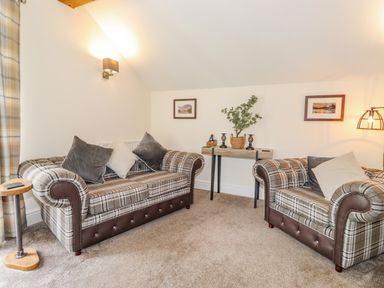 A living room with two plaid sofas a wooden side table and a console table with plants and candle holders at Chestnuts Cottage in Windermere