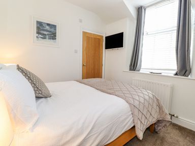 A bedroom with a bed pillow blanket a wooden door a wall mounted television and a window with curtains at Chestnuts Cottage in Windermere